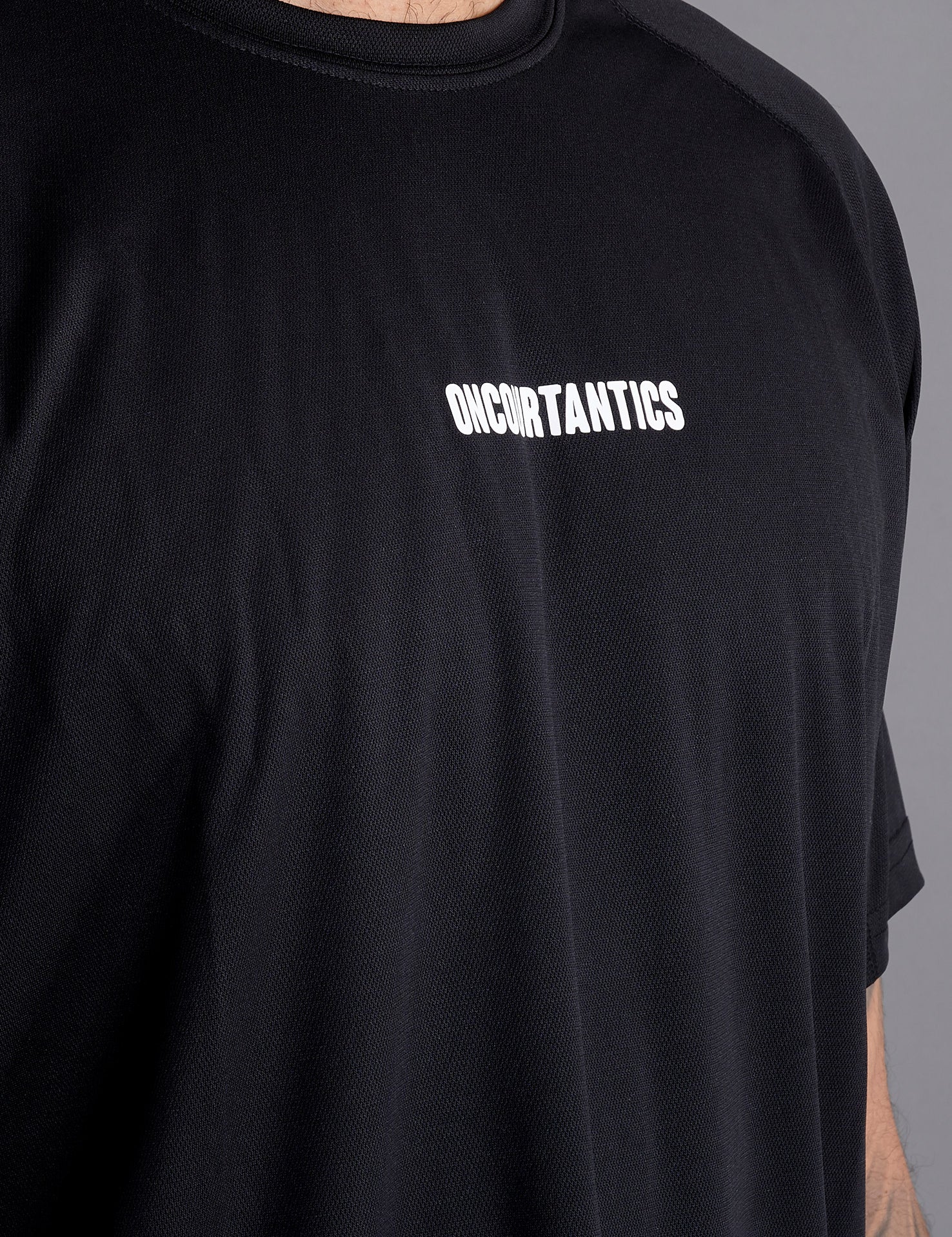 Close-up of ONCOURTANTICS black performance t-shirt fabric and small chest logo detail, highlighting lightweight, breathable material.