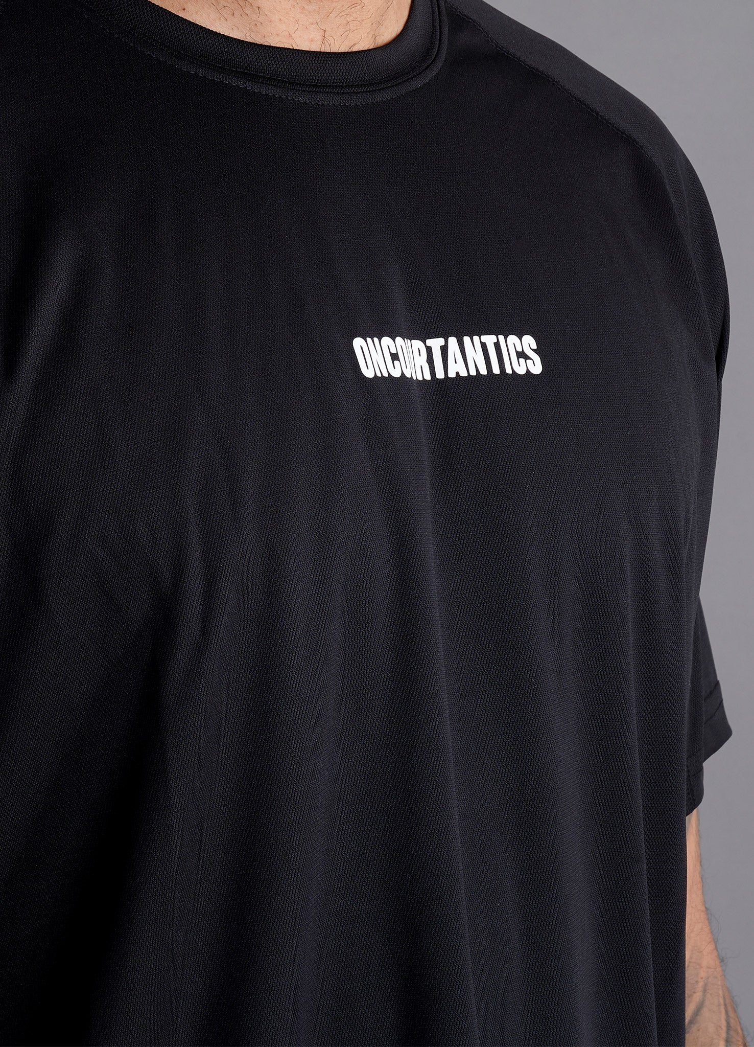 Close-up of ONCOURTANTICS black performance t-shirt fabric and small chest logo detail, highlighting lightweight, breathable material.