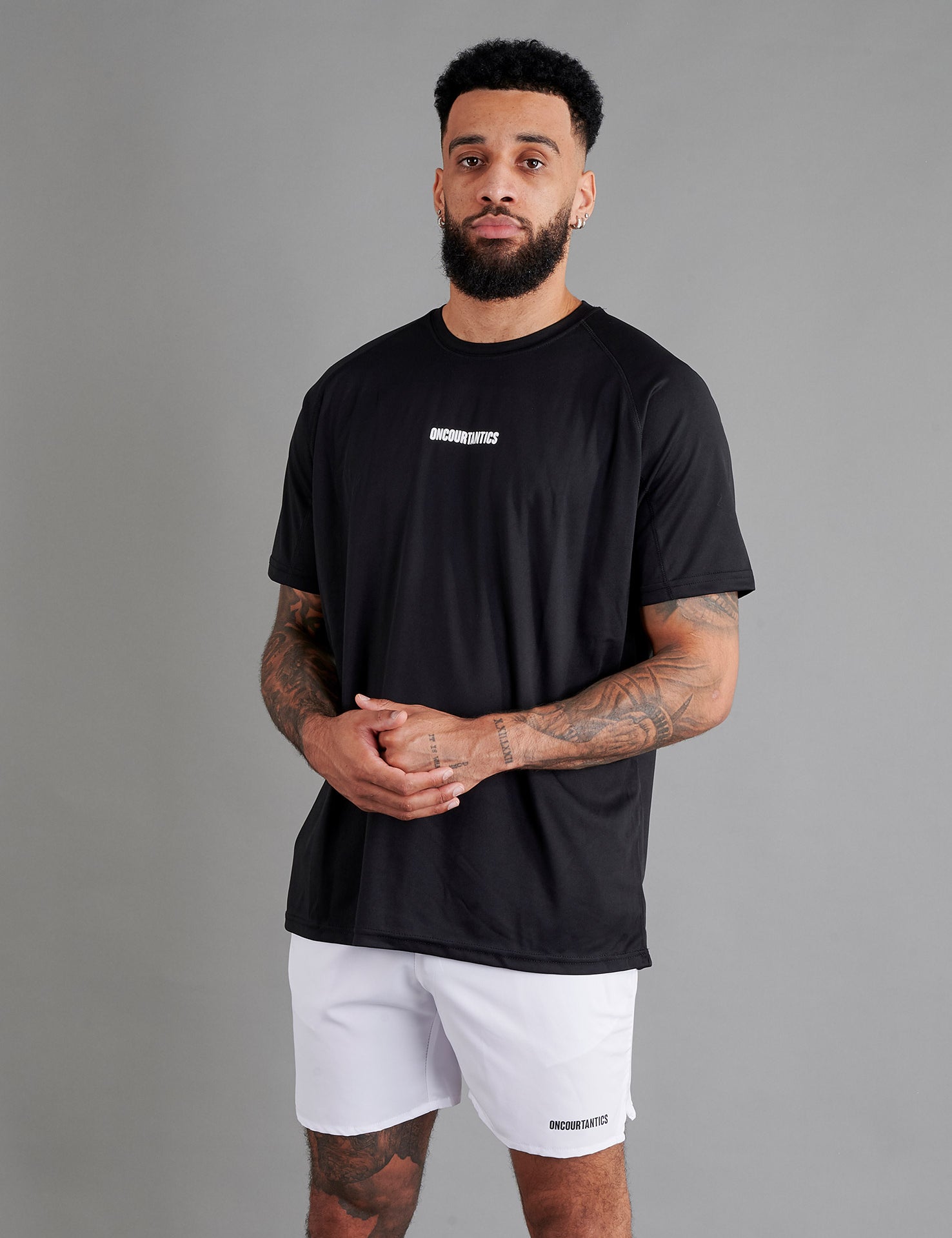 Male basketball model wearing ONCOURTANTICS black performance t-shirt with small chest logo, paired with white shorts, front-facing against plain grey background.