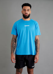 Male basketball model wearing ONCOURTANTICS blue performance t-shirt with small chest logo, paired with black shorts, front-facing against plain grey background.