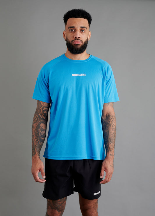 Male basketball model wearing ONCOURTANTICS blue performance t-shirt with small chest logo, paired with black shorts, front-facing against plain grey background.
