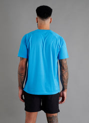Rear view of male model in ONCOURTANTICS blue performance t-shirt with small chest logo, black shorts, standing on grey background