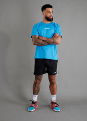 Male basketball model wearing ONCOURTANTICS blue performance t-shirt with small chest logo, paired with black shorts, front-facing against plain grey background.