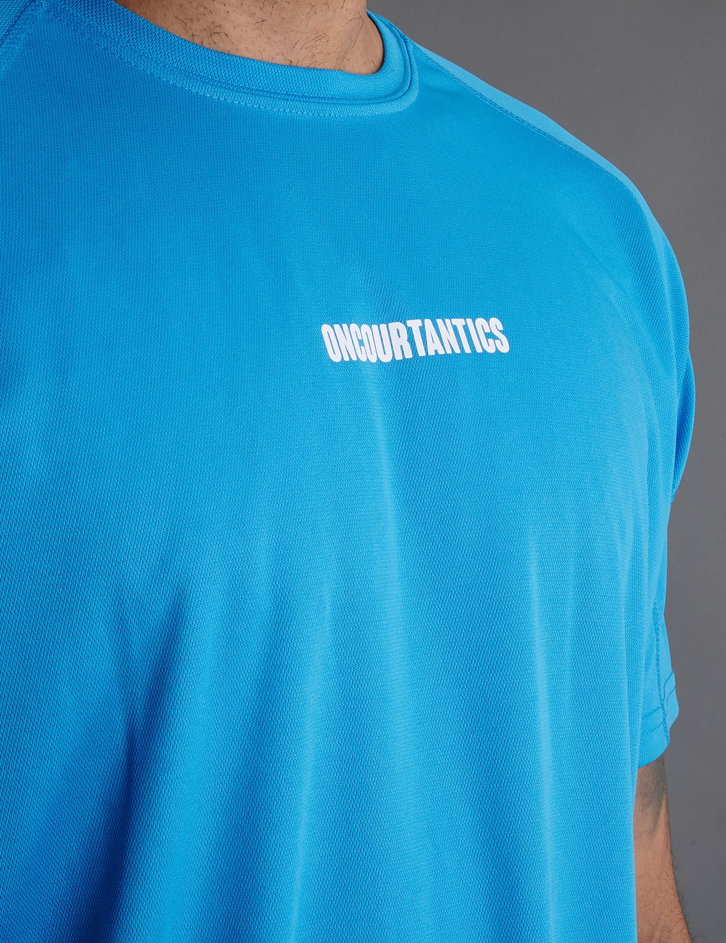 Close-up of ONCOURTANTICS blue performance t-shirt fabric and small chest logo detail, highlighting lightweight, breathable material