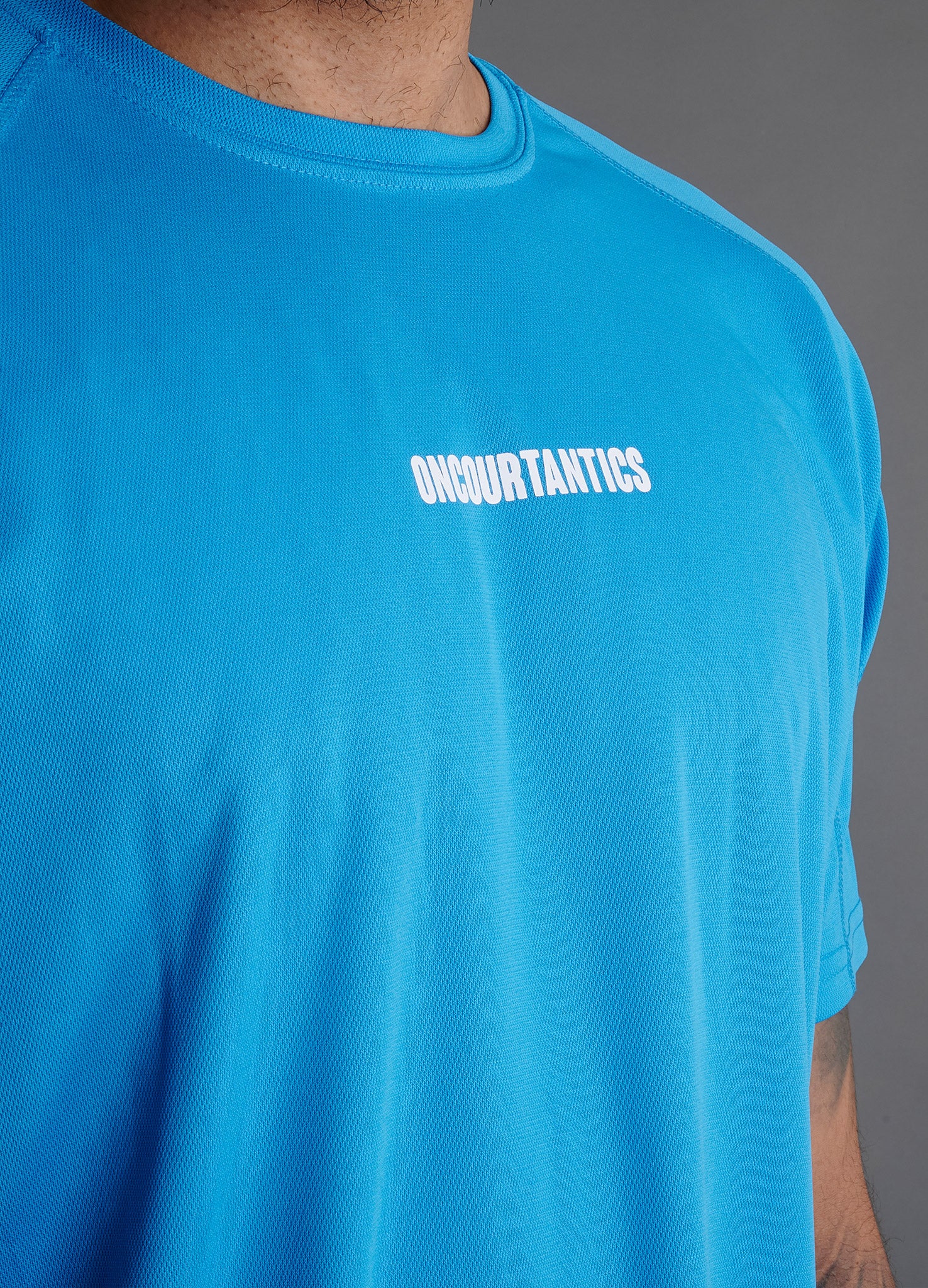Close-up of ONCOURTANTICS blue performance t-shirt fabric and small chest logo detail, highlighting lightweight, breathable material
