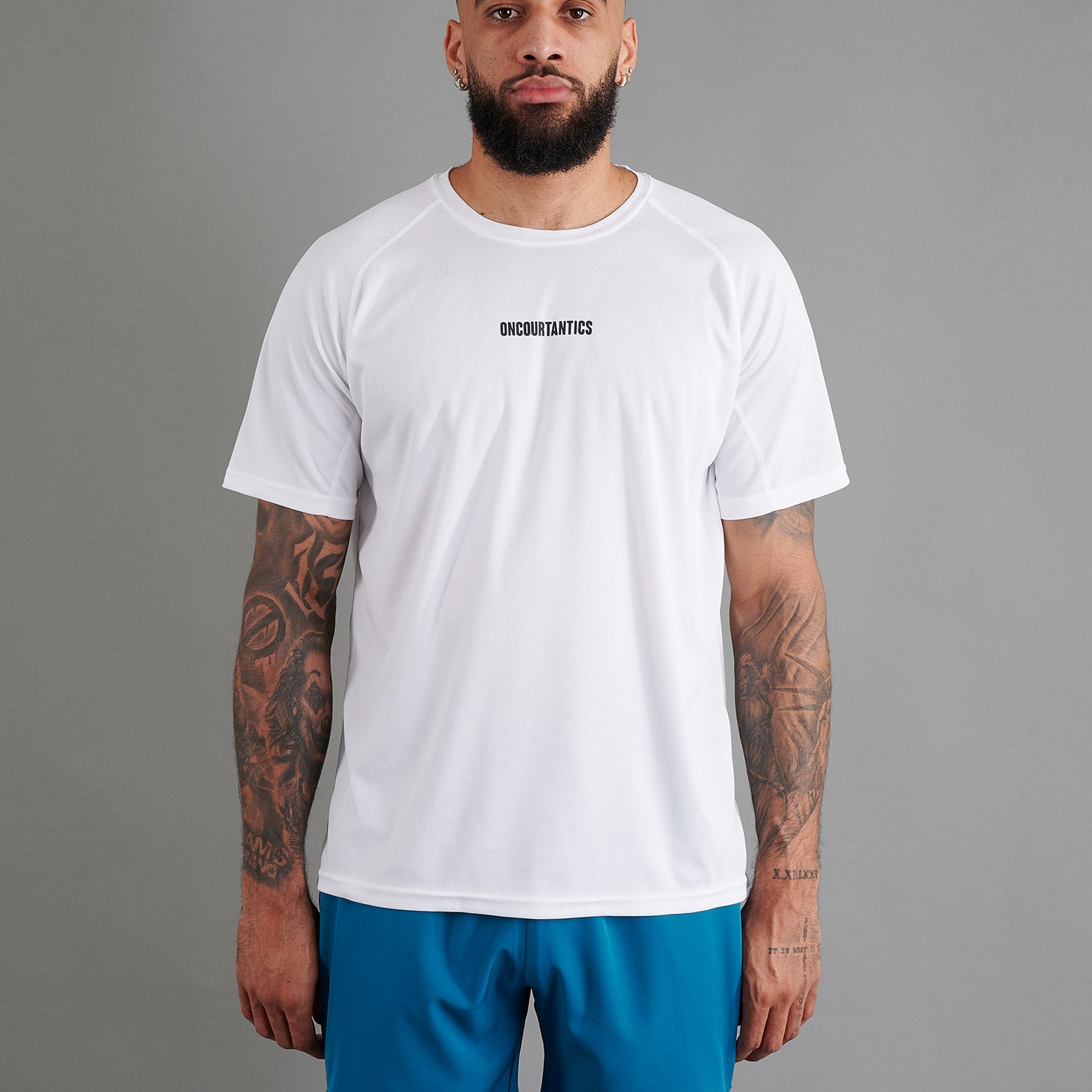 Male basketball model wearing ONCOURTANTICS White performance t-shirt with small chest logo, paired with teal shorts, front-facing against plain grey background.