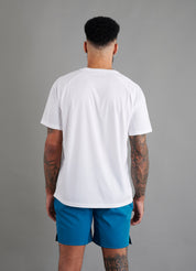 Rear view of male model in ONCOURTANTICS white performance t-shirt with small chest logo, teal shorts, standing on grey background.