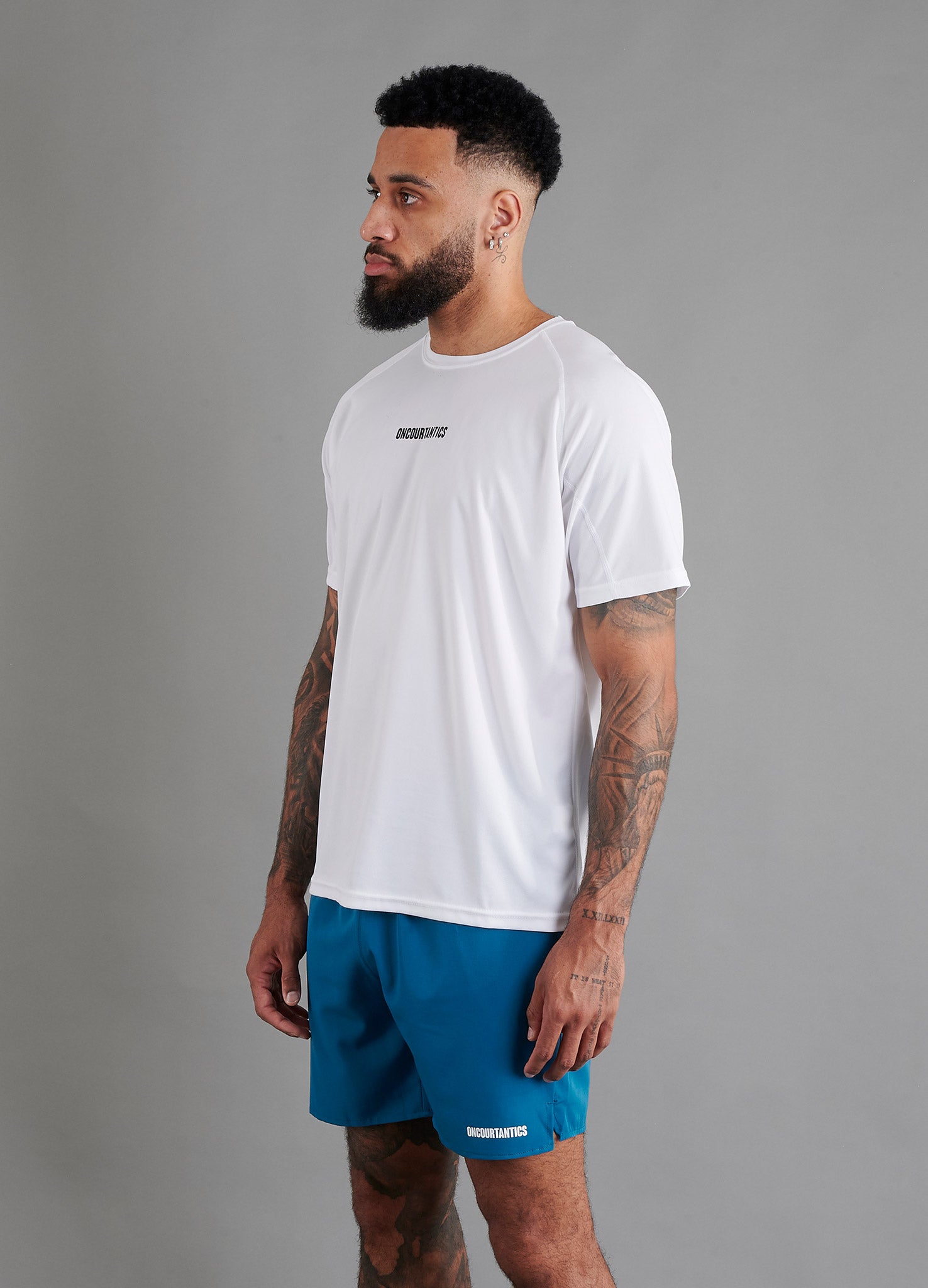 Side view of male basketball model wearing ONCOURTANTICS White performance t-shirt, showing athletic fit and short sleeves, styled with Teal shorts.