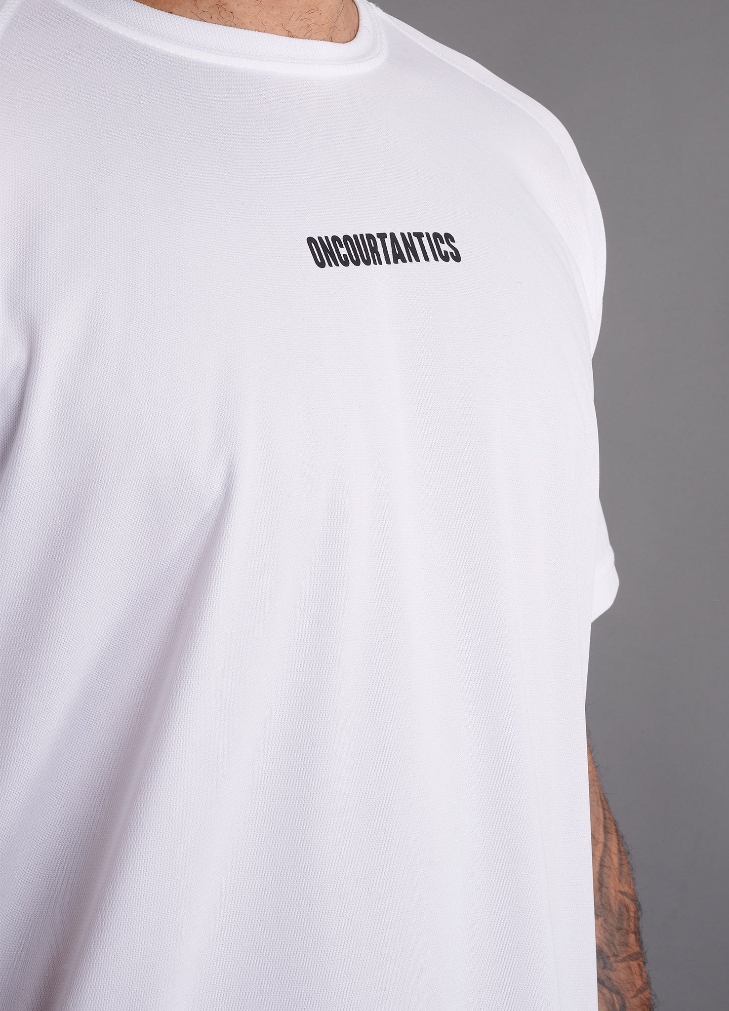 Close-up of ONCOURTANTICS White performance t-shirt fabric and small chest logo detail, highlighting lightweight, breathable material.